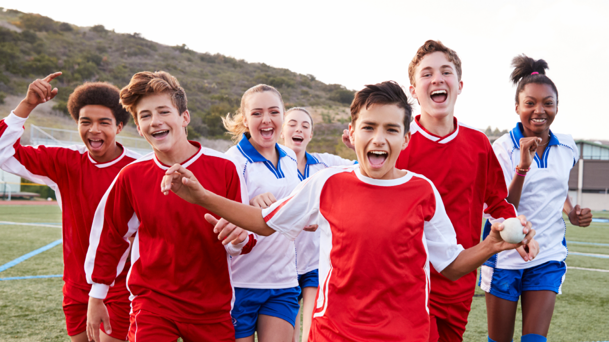 Happy teenagers running in red and white sports shirts outside 